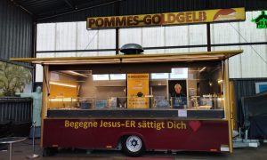 Foodtruck „Pommes Goldgelb“ in Verden mit dem Schriftzug „Begegne Jesus – Er sättigt Dich“ und Blick auf den Verkaufsstand.