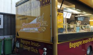 Pommes-Foodtruck „Pommes Goldgelb“ in Verden mit evangelischer Aufschrift „Begegne Jesus – Er sättigt Dich“ und Blick in den Verkaufsbereich.