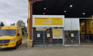 Eingang und Lieferwagen der evangelischen Pommesbude „Pommes Goldgelb“ in Verden mit gelber Beschilderung.