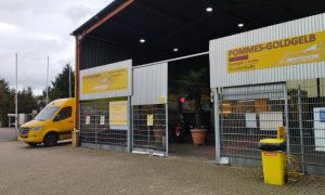 Außenansicht der evangelischen Pommesbude „Pommes Goldgelb“ in Verden mit gelber Beschilderung und Lieferfahrzeug.